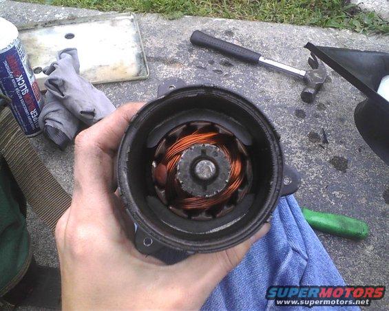 Hand holding a disassembled motor part with copper windings. Tools and gloves nearby