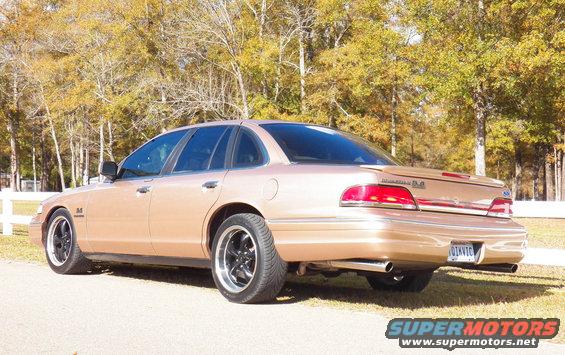 Rear view of a tan Ford Crown Victoria with aftermarket wheels. It has a spoiler and dual exhaust