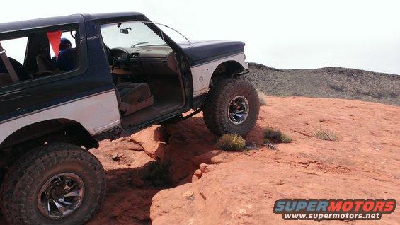 Two-tone blue and white Ford Bronco with lifted suspension on rocky terrain