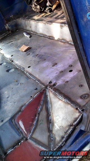 Interior floor of a vehicle with metal patches welded in place. Some patches are red, others are bare metal