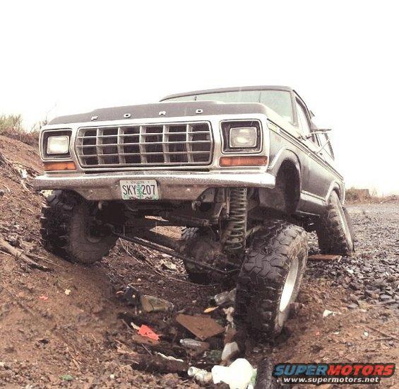Dark 1978 Ford Bronco with lifted suspension and large tires, angled on a dirt incline with debris