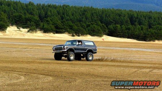 Dark SUV with lifted suspension on sandy terrain, front grille visible