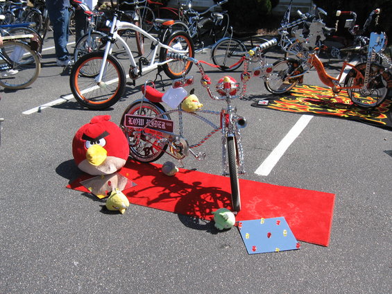 Custom lowrider bicycle with 'LOW RIDER' plate, red carpet, and Angry Bird plush toy. Other bicycles visible in background