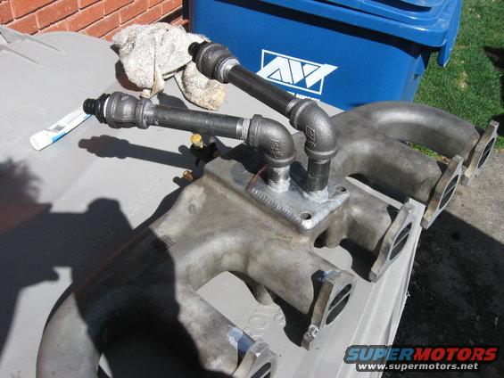 Custom intake manifold with pipes and fittings attached, sitting on a gray surface