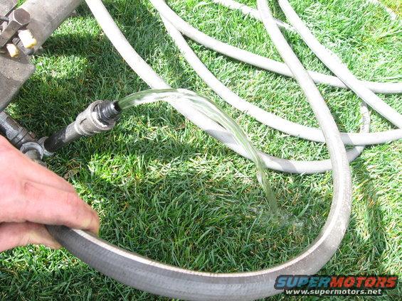 Water flows from a black hose fitting into a larger grey hose on green grass