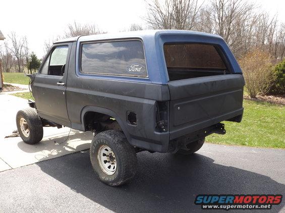 1981 Ford Bronco with blue top and black body, lifted on off-road tires, parked on driveway