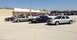 2005 Ford Crown Victoria - Several Ford Crown Victorias, some appearing to be police cruisers, are parked in a lot outside a store.