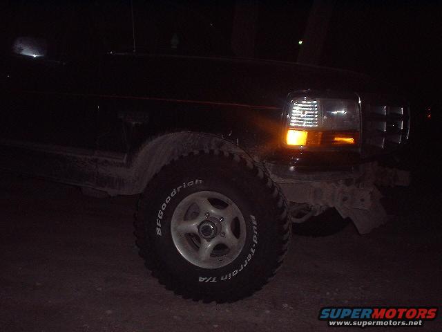 Black Ford Bronco front fender and tire, with headlight on. The vehicle appears to be from the early 1990s