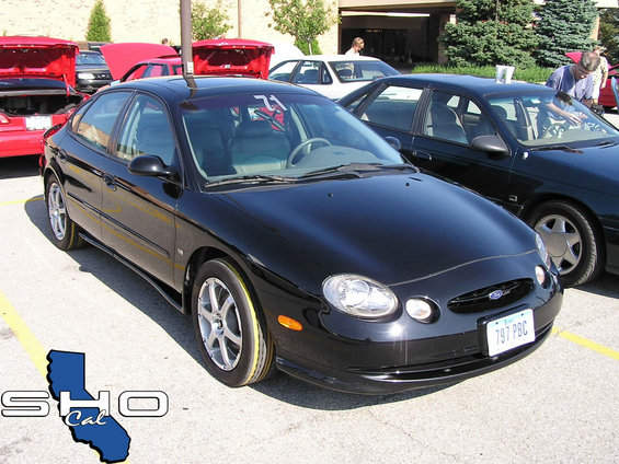 Black Ford Taurus with yellow tire markings, parked at an outdoor event