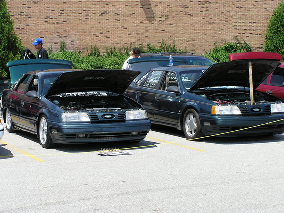 Two dark green 1993 Ford Taurus sedans with hoods open, front view