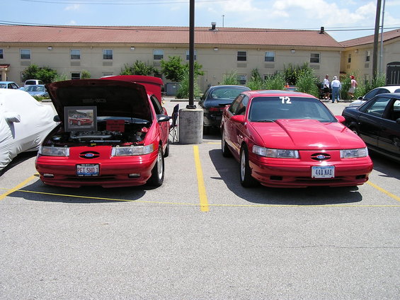 Two red 1993 Ford Taurus cars parked in a lot, one with hood open