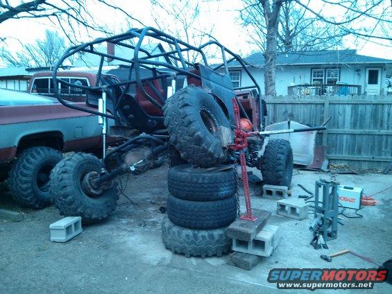 Custom off-road buggy frame on tires with a pickup truck next to it
