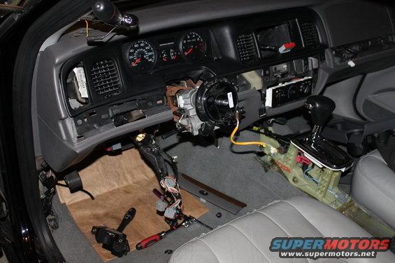 Car interior with dashboard and steering column removed, showing wiring and components