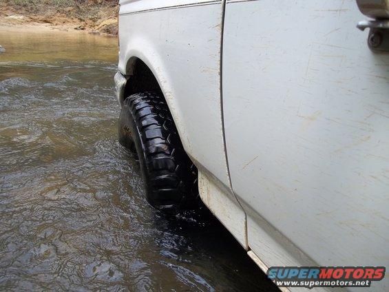 White SUV's front tire in shallow water. Side panel and door visible