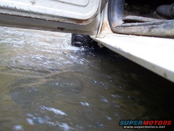 White vehicle door open, tire in water, rust on door frame