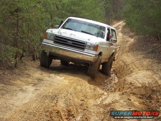White 1990 Ford Bronco navigating a muddy off-road trail