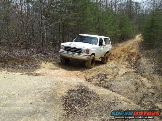 White 1990 Ford Bronco driving on a dirt trail through trees