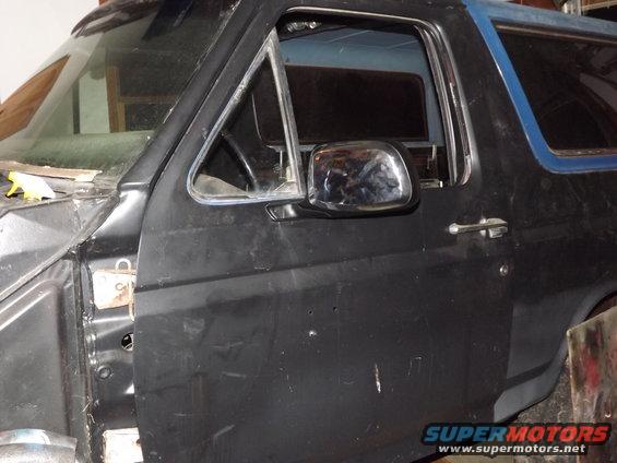 Black Ford Bronco door and fender, showing chrome mirror and door handle. The vehicle appears to be undergoing restoration