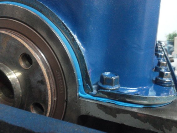 Close-up of a blue painted engine component with sealant and bolts