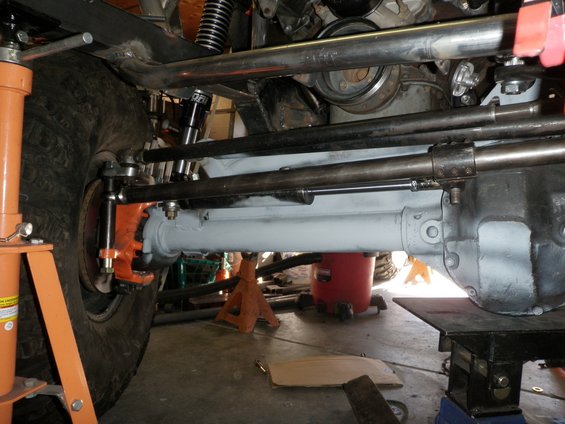 Close-up of vehicle's front axle, steering linkage, and suspension parts. A large tire is visible on the left