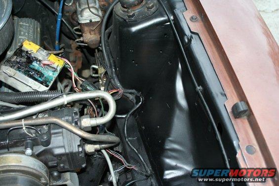 Close-up of a damaged electronic control module with exposed wires and circuit board, connected to engine bay wiring