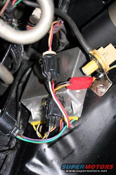Close-up of automotive wiring harness with black connectors, red electrical tape, and a silver box