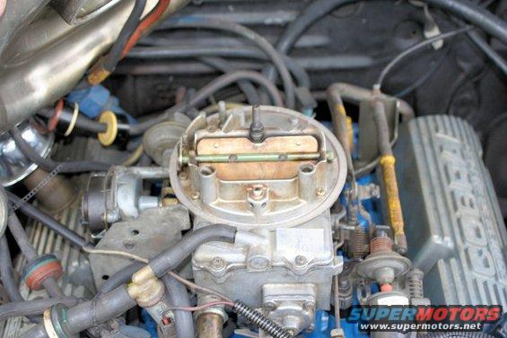 Close-up of a carburetor on a blue engine block with various hoses and wires