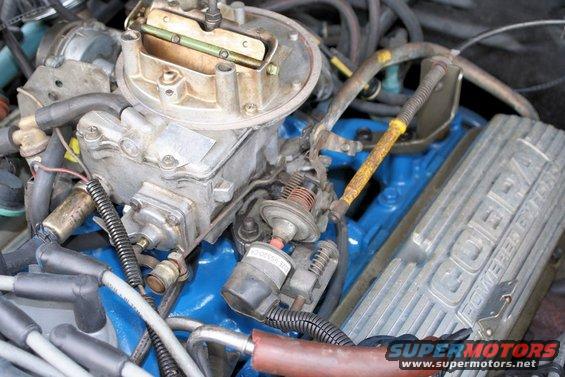 Close-up of engine parts including a carburetor and a silver valve cover with "COBRA POWERED BY" text