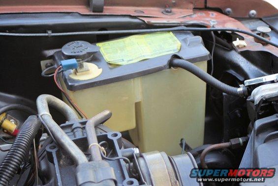 Windshield washer fluid reservoir with yellow warning sticker and hoses connected