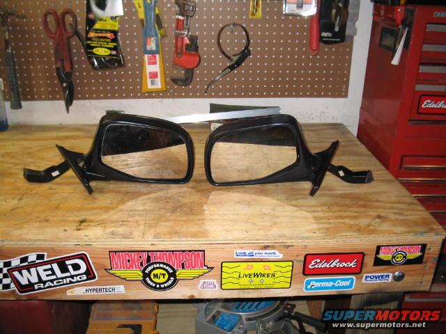 Two black side mirrors on a wooden workbench with various stickers