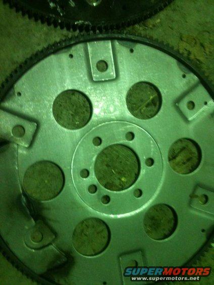 Close-up of a metal flywheel with circular cutouts and bolt holes