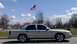 2008 Mercury Grand Marquis - A silver sedan is parked outdoors under a bright sky with an American flag flying above.