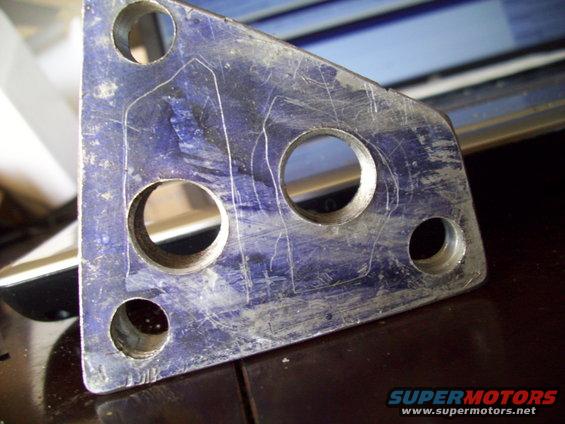 Blue metal bracket with four holes and scribe lines, showing scratches and wear