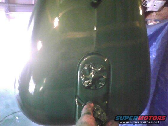 Green painted fuel tank with a circular emblem on it. A hand is holding a spray gun near the bottom