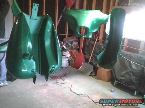 Green motorcycle fairings hanging in a garage, some parts on the floor