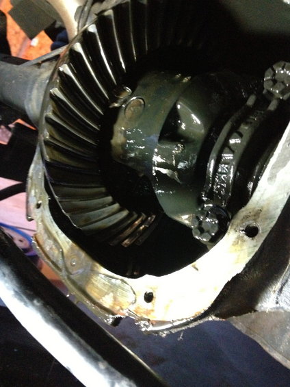 Close-up of differential gears with dark lubricant. Some text is visible on one of the gears