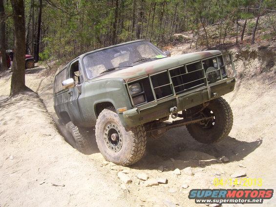 Olive drab off-road SUV with custom grille guard climbing a dirt hill, another red SUV visible in background