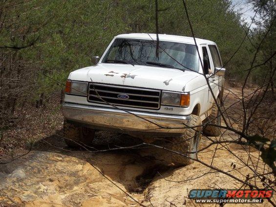 White Ford Bronco II driving on a dirt trail through trees
