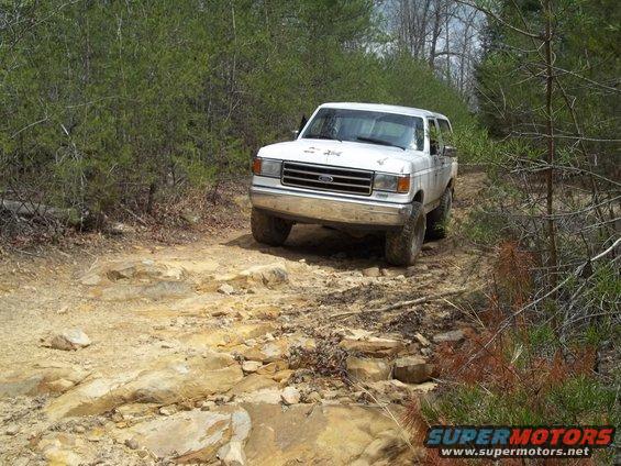 White Ford Bronco driving on a rocky, wooded trail