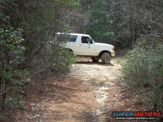 White 1990 Ford Bronco driving off-road on a dirt path