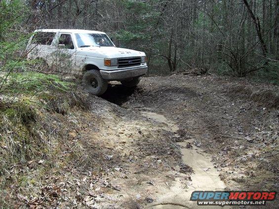 White SUV on a muddy trail, front 3/4 view, tires on dirt embankment