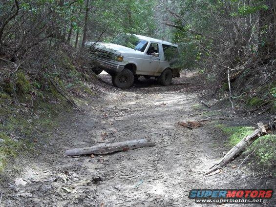 White 1990 Ford Bronco on a muddy, wooded trail, angled to the left