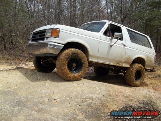 White 1990 Ford Bronco with large off-road tires on a dirt trail