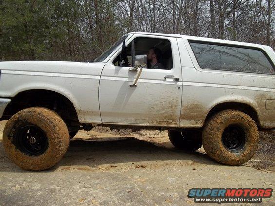 White Ford Bronco with mud on tires driving on a dirt road
