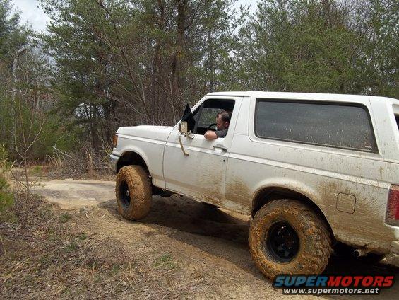 White Ford Bronco with mud-splattered body and large off-road tires driving on a dirt path