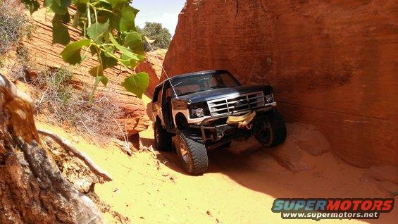 Black Ford Bronco off-roading in a sandy canyon, front bumper damaged