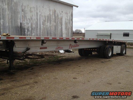 Flatbed trailer with "Revolution" text, parked on dirt near a barn