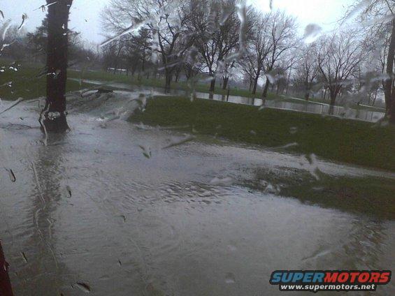 Flooded park with trees and grass, viewed through a wet window