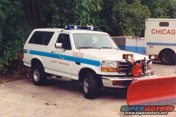 1994 Ford Bronco with blue light bar and front snow plow, marked 'PROPERTY MANAGEMENT' and '6835'. Another vehicle with 'CHICAGO' visible is parked behind