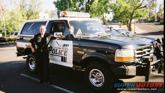 Black and white Ford Bronco police SUV with "LAKEPORT POLICE" text, parked on asphalt with a uniformed officer standing beside it